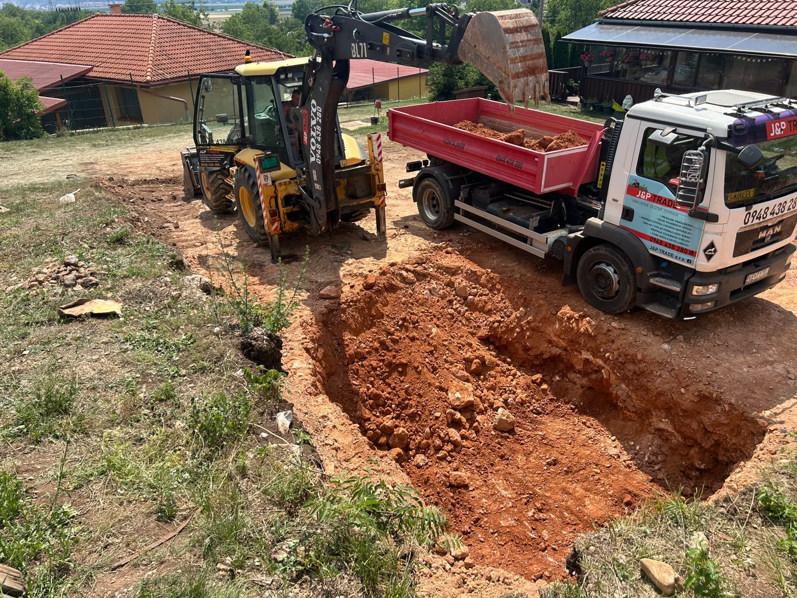 Dve nákladné vozidlá J&P TRADE, sklápač s kontajnerovou korbou a vozidlo s hydraulickou rukou HIAB, pripravené na stavenisku